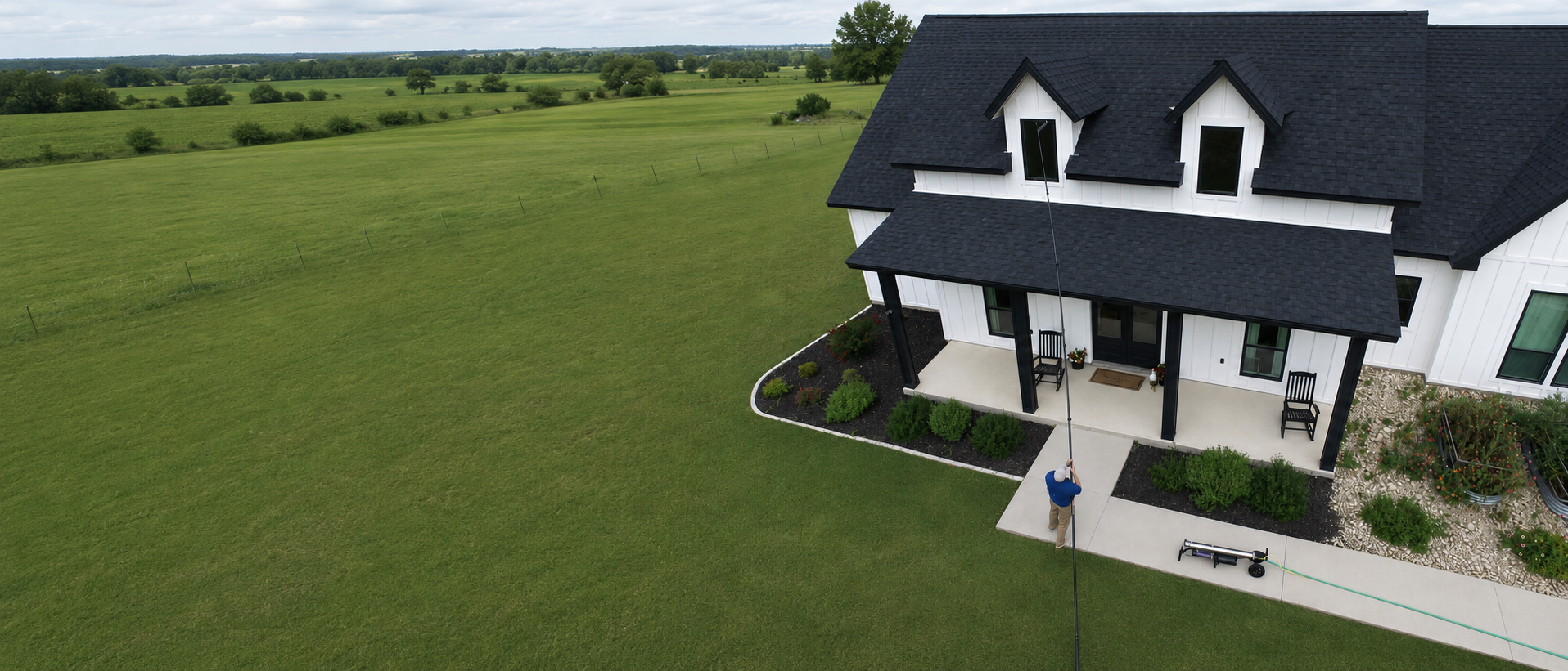 A technician cleaning the windows of a Central Texas farmhouse from the ground with a water-fed pole