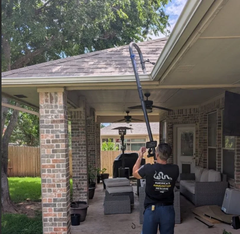 Technician using a ground-based gutter vacuum system to clear debris from a home's gutters